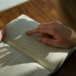 person reading book on brown wooden table taken at daytome